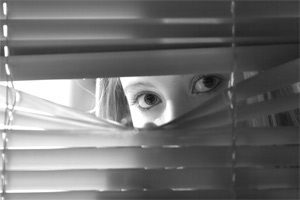 fearful woman peering through blinds